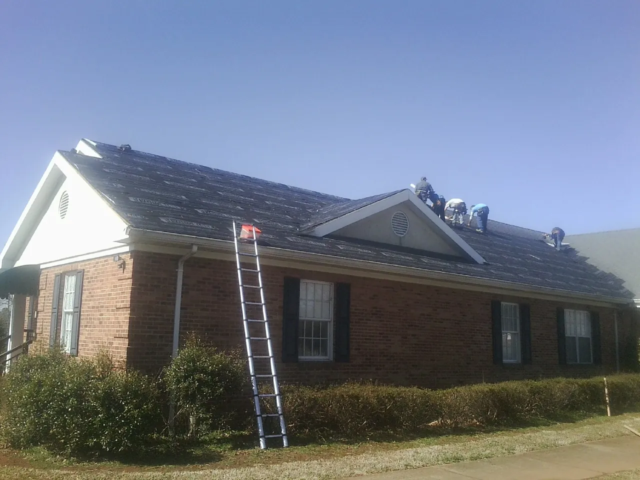 Crew tearing shingles off a brick ranch roof with a ladder set — Metal Roof Repair work by our crew in Saint Francis